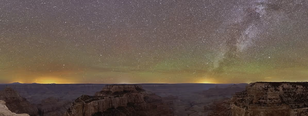 Star-filled night sky with the Milky Way visible above the dark silhouette of the Grand Canyon at dusk.